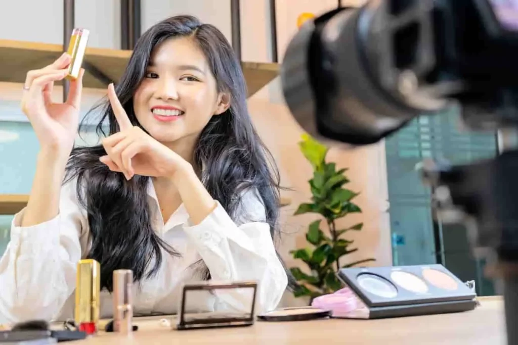 Youtubeuse en pleine vidéo tuto, rouge à lèvres à la main, palette et miroir sur table, ambiance créative et professionnelle.