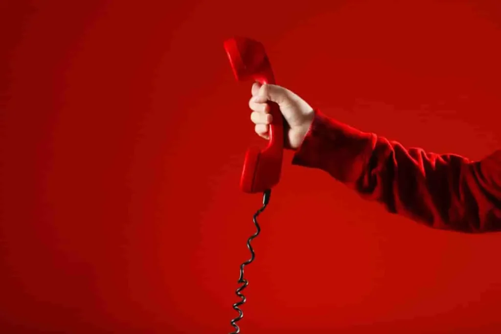 Combiné rouge tendu vers l’avant, symbolisant le démarchage téléphonique d’UNADEV et l’appel direct aux donateurs.