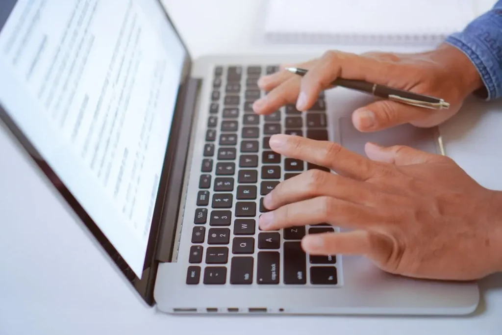 Mains tapant sur clavier avec stylo en main, image d’un contenu structuré pour booster la lisibilité grâce aux bullet points