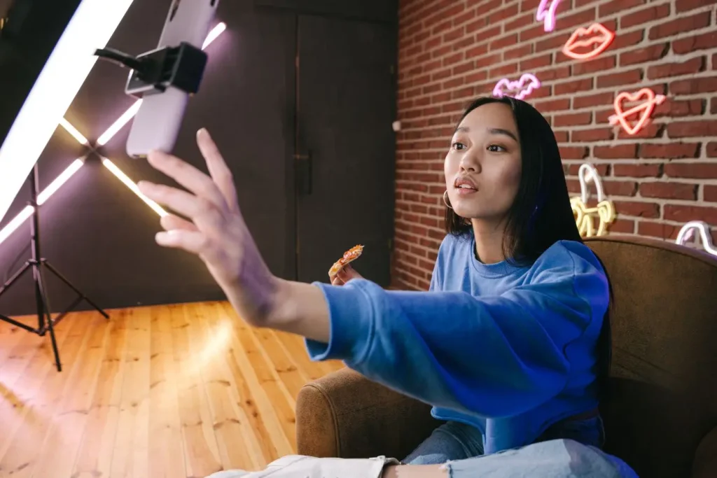 Personne en sweat bleu devant mur à néons, tenant une pizza et interagissant avec téléphone, ambiance cross-posting