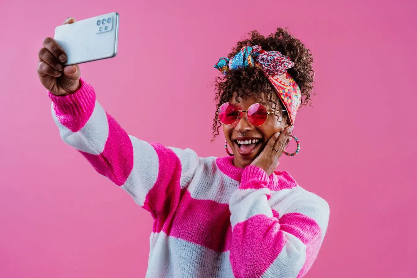 Personne souriante en tenue rose prenant un selfie illustrant une pose typique avec filtre Snapchat