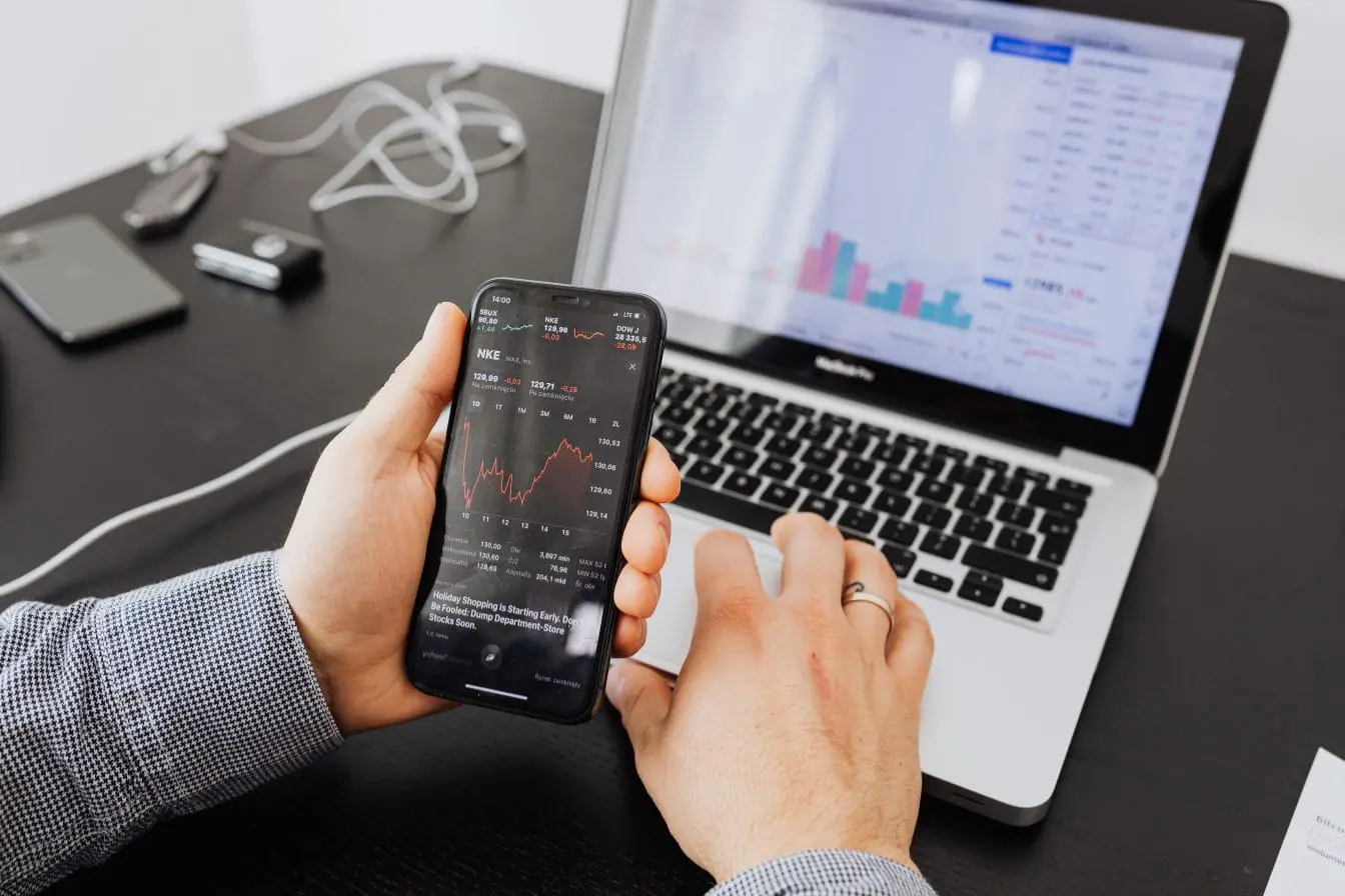 Personne analysant données boursières sur smartphone et ordinateur, image illustrant la mesure du ROI d’une campagne marketing via indicateurs financiers