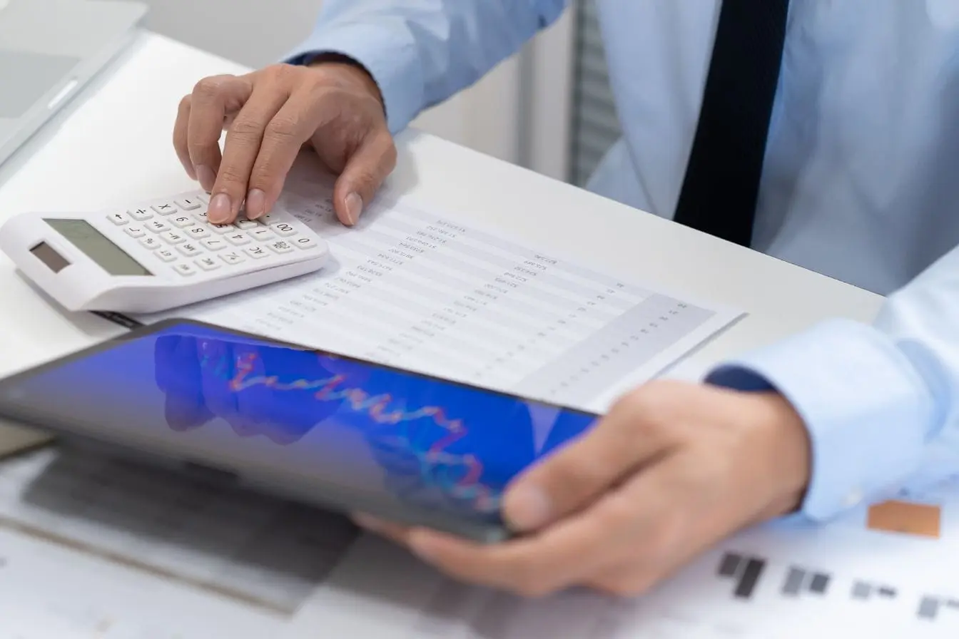 Personne en tenue professionnelle utilisant calculatrice et tablette avec graphique coloré illustrant analyse du churn rate dans un contexte financier.