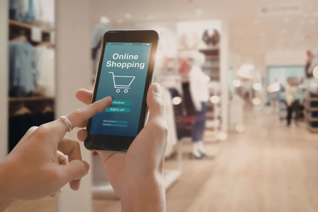 Personne tenant un smartphone affichant interface Shopify avec panier et options de commande dans un magasin de vêtements illustrant la création d’une boutique en ligne.