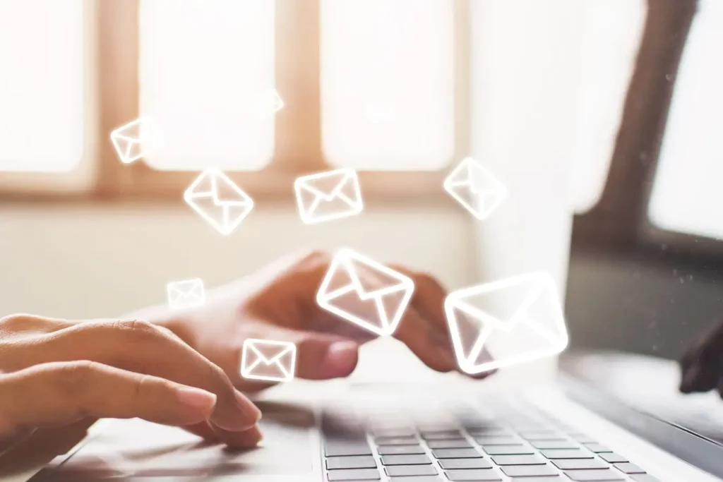 Mains tapant sur clavier d’ordinateur avec icônes d’enveloppes flottantes, image illustrant la création d’une newsletter performante qui convertit.