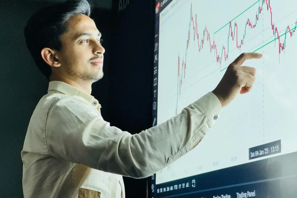 Personne pointant un graphique de trading sur écran géant, image illustrant l’affiliation marketing et l’analyse des performances en ligne.