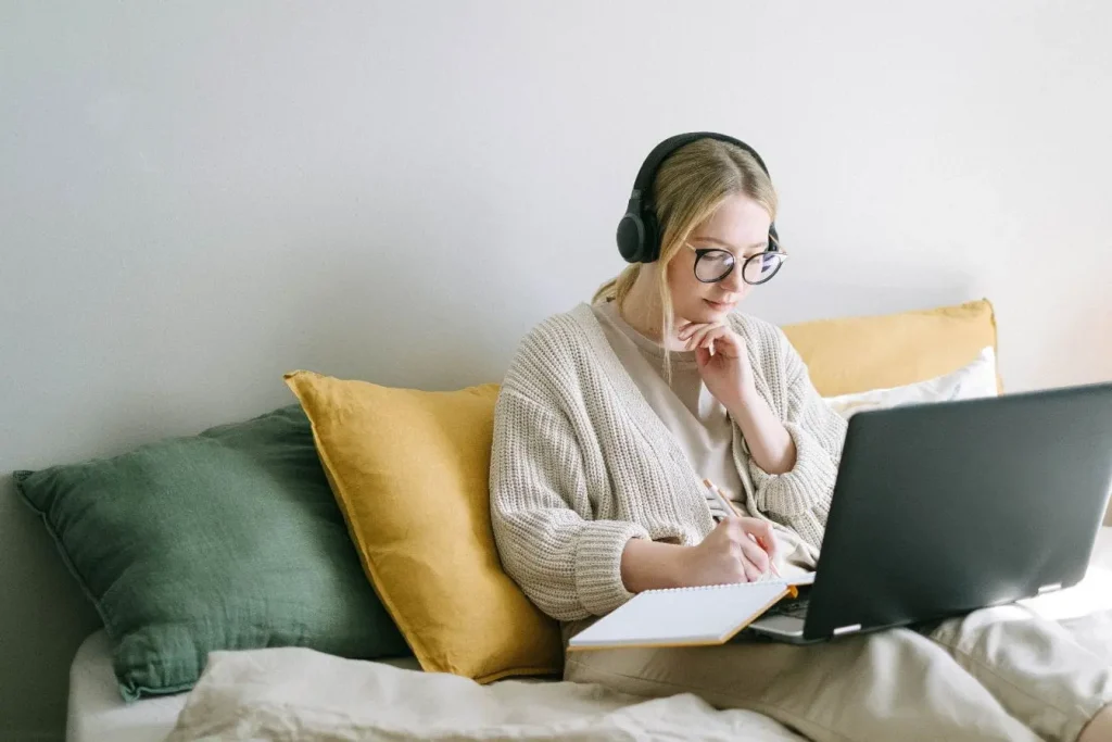 Personne assise sur lit avec ordinateur portable et carnet, image illustrant le travail de copywriting dans un cadre cosy et inspirant.
