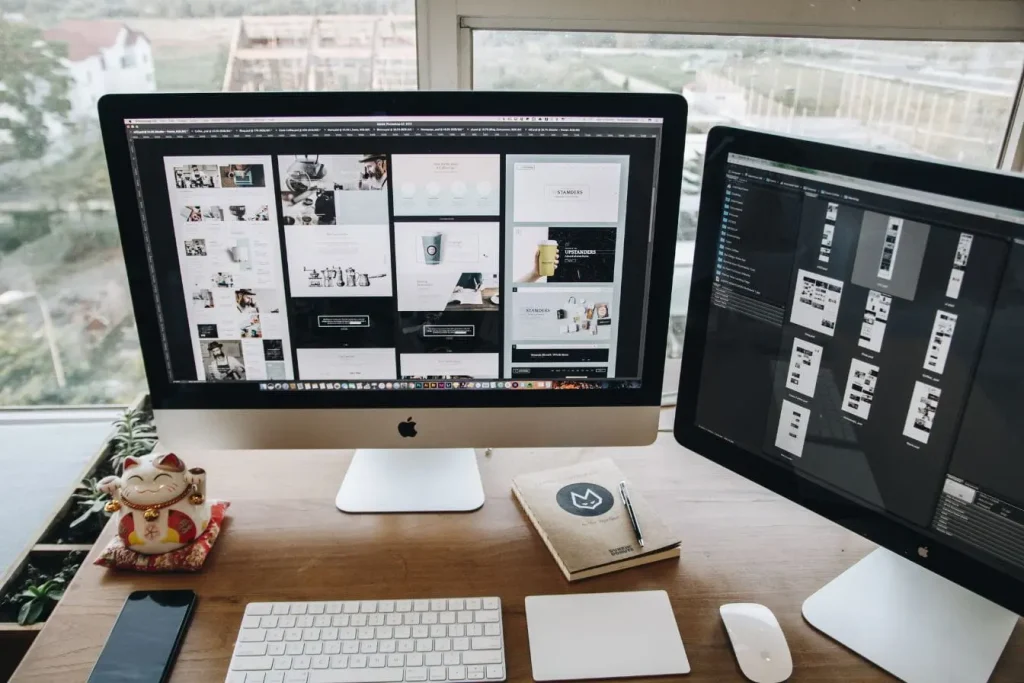 Bureau moderne avec deux grands écrans affichant maquettes web et gestion de projets, illustrant un espace de design simplifié pour non-designers.