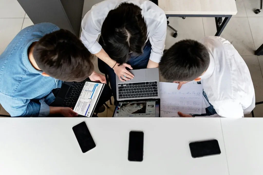 Groupe collaborant sur un projet avec laptops et diagrammes, reflet de l’architecture microservices qui segmente les fonctions pour plus de flexibilité.