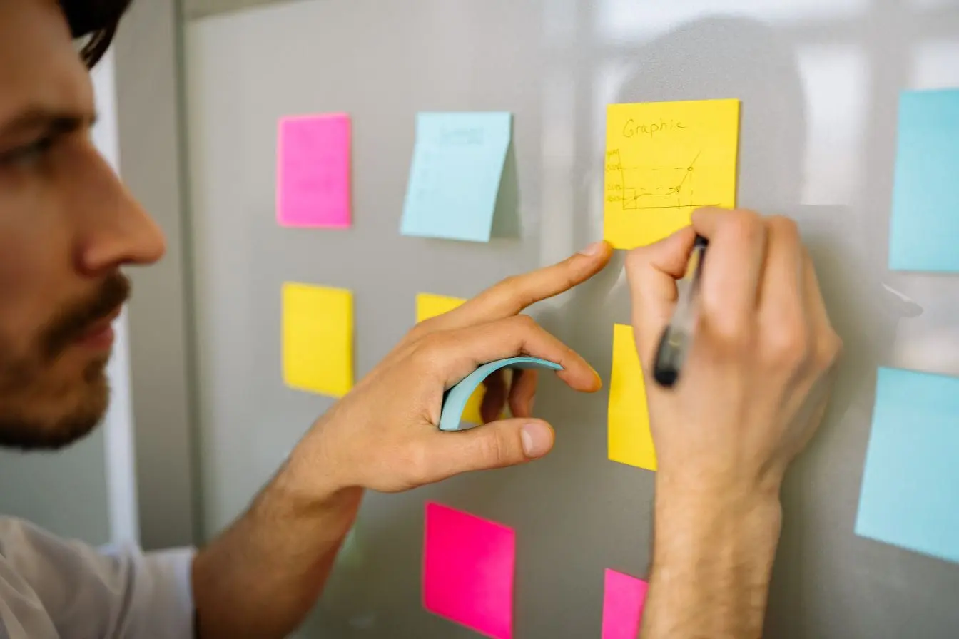 Main écrivant un graphique sur post-it jaune entouré de notes colorées, image d’un atelier de design thinking centré sur l’idéation visuelle.