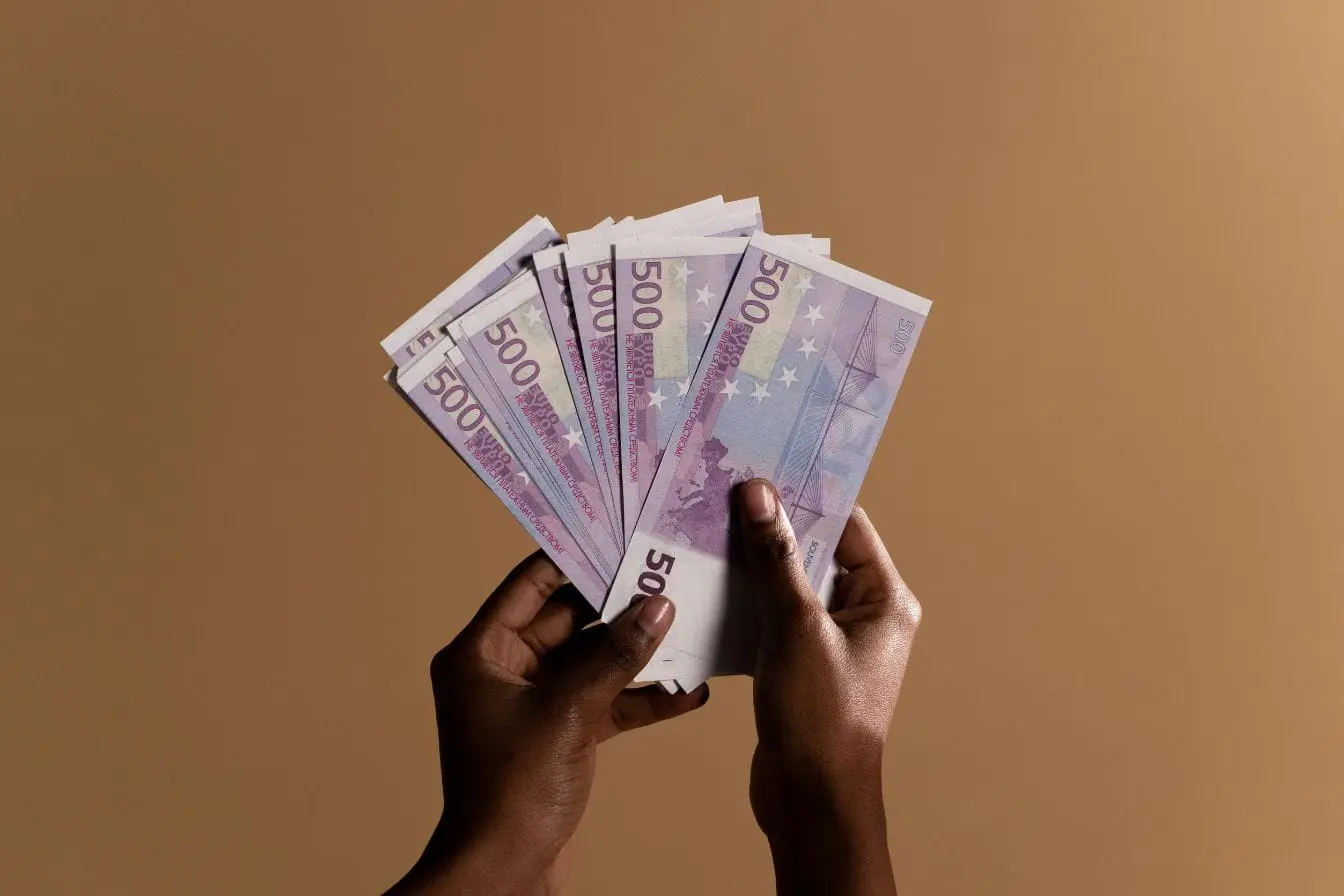 Mains tenant plusieurs billets de 500 euros, image illustrant l’économie des abonnements et la circulation d’argent liée aux services récurrents.