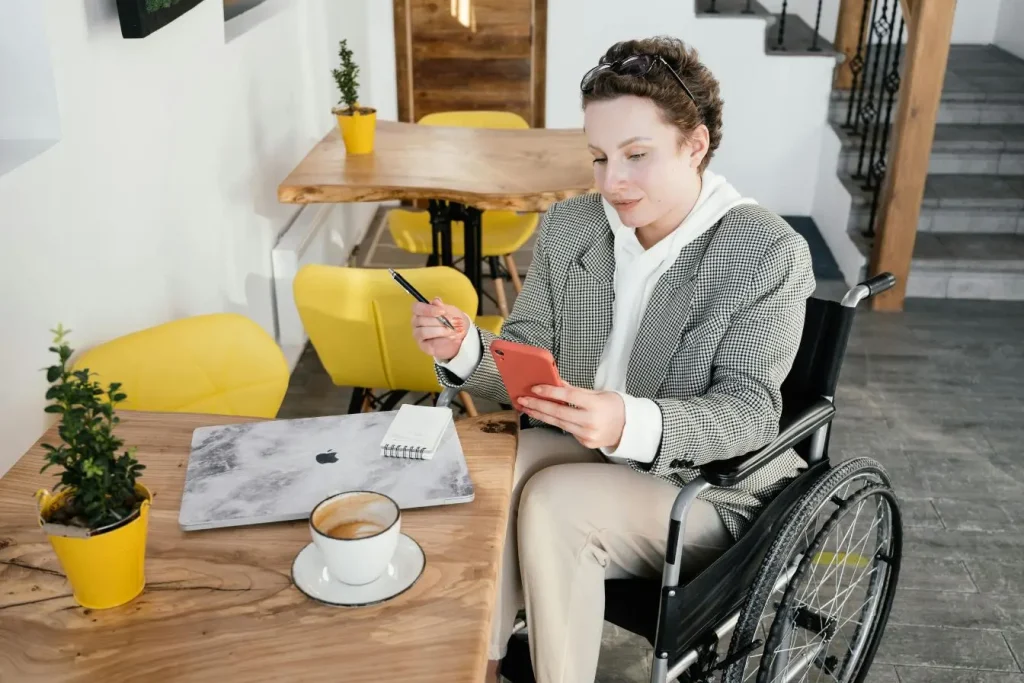 Personne en fauteuil roulant travaillant sur ordinateur portable, image illustrant l’accessibilité numérique dans un espace moderne.