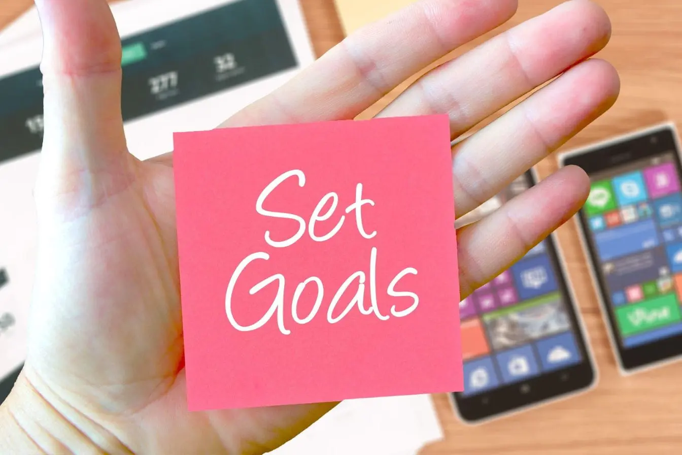 Main tenant post-it rose marqué Set Goals, image représentant la méthode OKR pour fixer objectifs clairs et résultats mesurables.