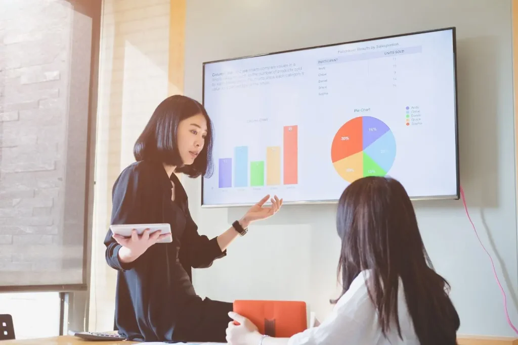 Deux personnes en réunion devant écran avec graphiques, image illustrant la méthode OKR pour fixer objectifs et résultats clés.