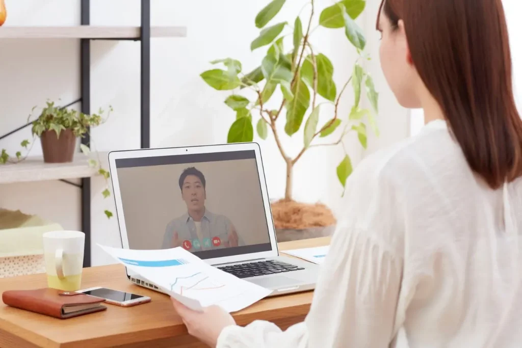 Bureau avec portable affichant un interlocuteur en visioconférence, représentant le management d’une équipe dispersée et la coordination virtuelle.