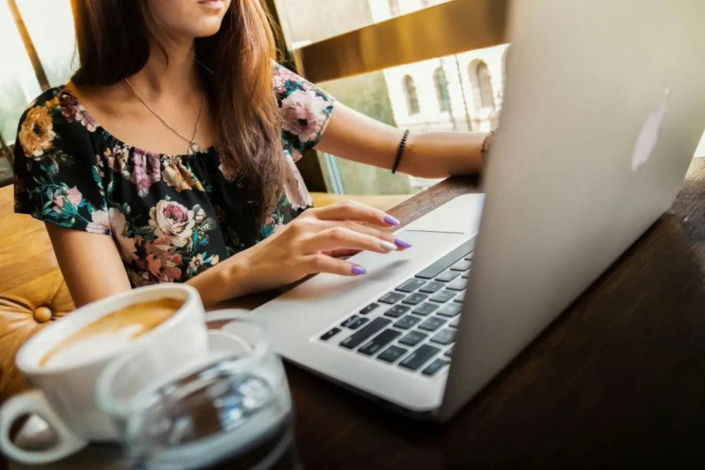 Personne en blouse fleurie travaillant sur laptop avec café, image illustrant la stratégie Product-Led Growth centrée sur expérience utilisateur.