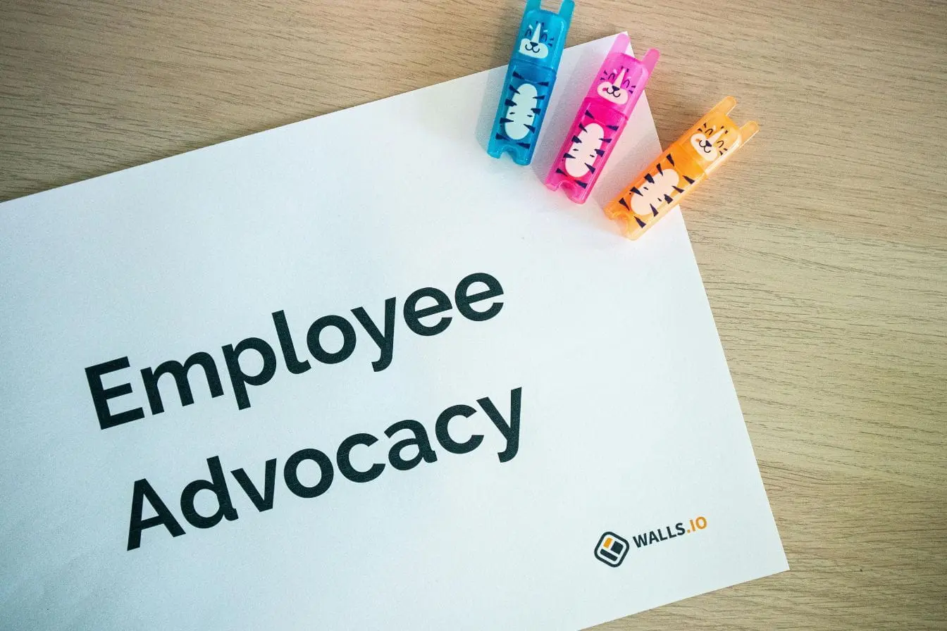 Feuille blanche avec titre Employee Advocacy et pinces colorées, image illustrant la valorisation des employés comme ambassadeurs de marque.