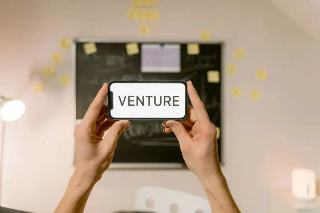 Mains tenant smartphone affichant venture, image illustrant la différence entre Business Angel et Venture Capital dans financement de projets.