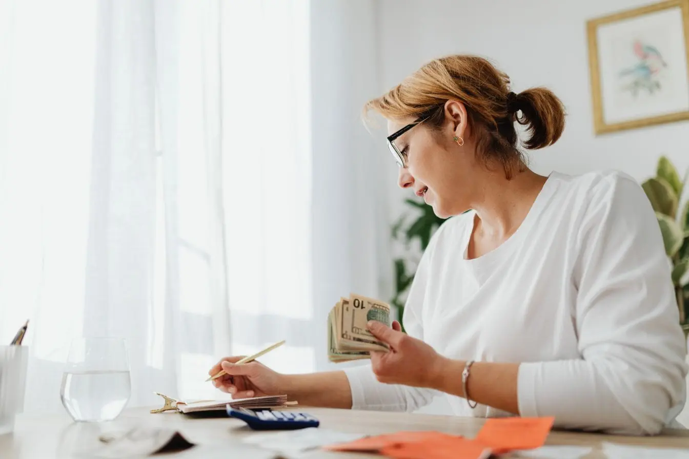 bootstrapping Personne tenant des billets tout en écrivant dans un carnet illustrant la gestion autonome des ressources financières typique du bootstrapping.