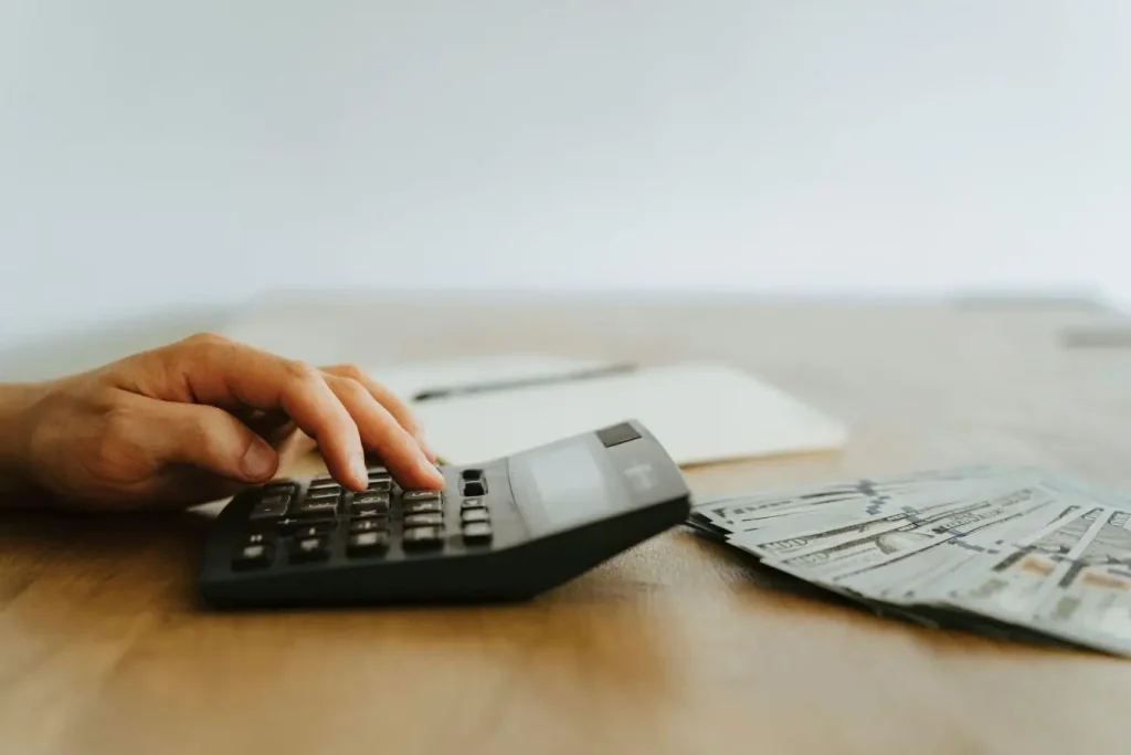 Main appuyant sur calculatrice avec billets de cent dollars reflétant la rigueur nécessaire pour calculer la valorisation d’une startup.