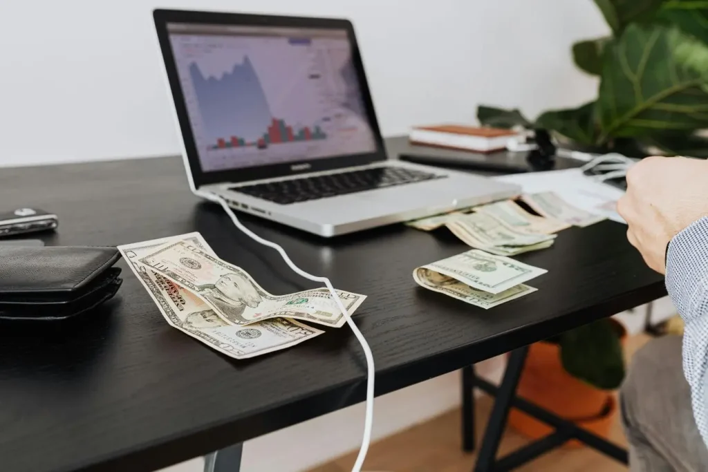 Bureau avec ordinateur affichant graphiques financiers et billets de banque reflétant la nécessité de calculer le burn rate pour suivre la trésorerie d’une startup.