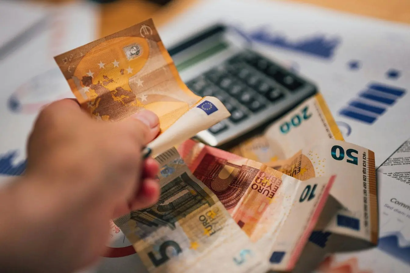calculer la valorisation d’une startup Main tenant billets d’euros devant calculatrice reflétant l’importance d’évaluer la valorisation d’une startup à partir de ses données financières.