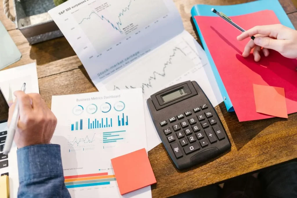 Mains tenant stylo devant graphiques financiers et calculatrice, image illustrant une cap table et la répartition du capital.