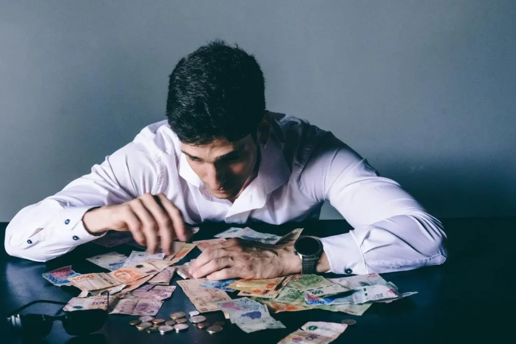 Personne en chemise blanche comptant billets et pièces sur table sombre, image illustrant une cap table et la répartition du capital.