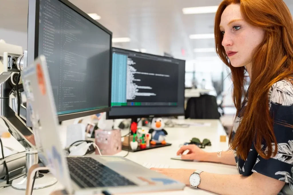 Personne concentrée devant plusieurs écrans affichant du code, image qui illustre l’application du framework Jobs to be Done dans un contexte technique.