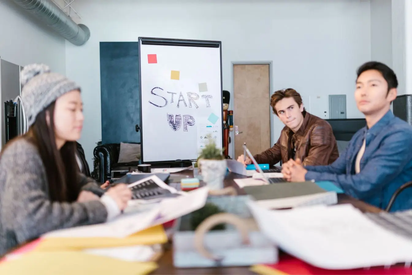 Lean Startup Trois personnes autour d’une table avec ordinateurs et documents, image qui illustre l’esprit Lean Startup et ses méthodes agiles.
