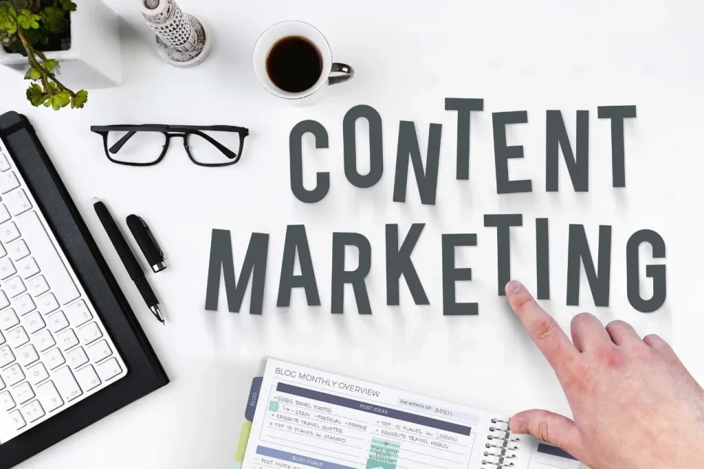 Bureau créatif avec carnet et clavier, main pointant vers contenu marketing, image d’une cohorte en marketing planifiant ses objectifs mensuels.