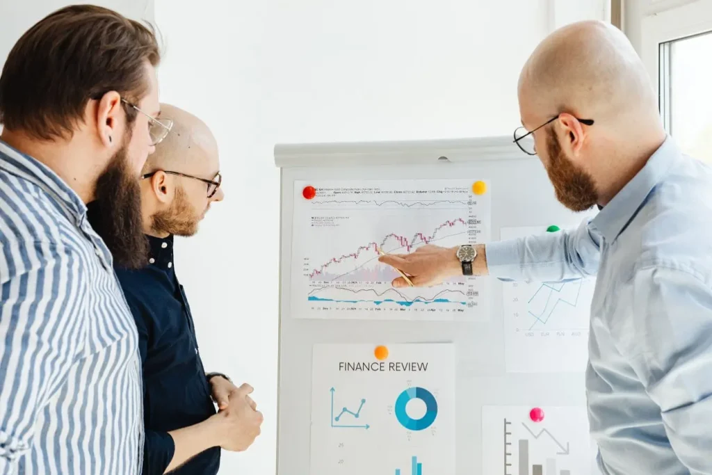 Trois personnes analysent graphiques financiers sur tableau, image illustrant la réflexion stratégique entre modèle freemium et premium.