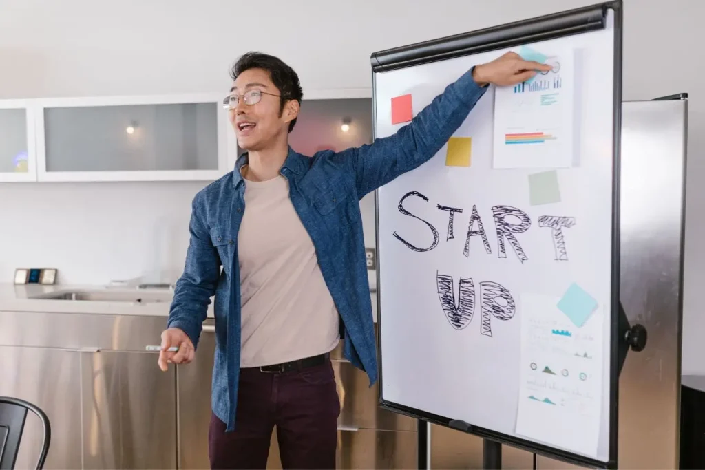 Personne en chemise bleue devant tableau blanc marqué START UP, image qui illustre la réflexion autour du pivot d’une startup.