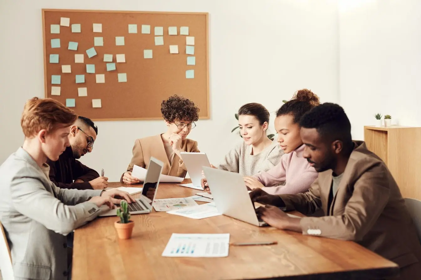 Équipe réunie autour d’une table avec ordinateurs et documents, image qui illustre la collaboration horizontale propre aux DAO.