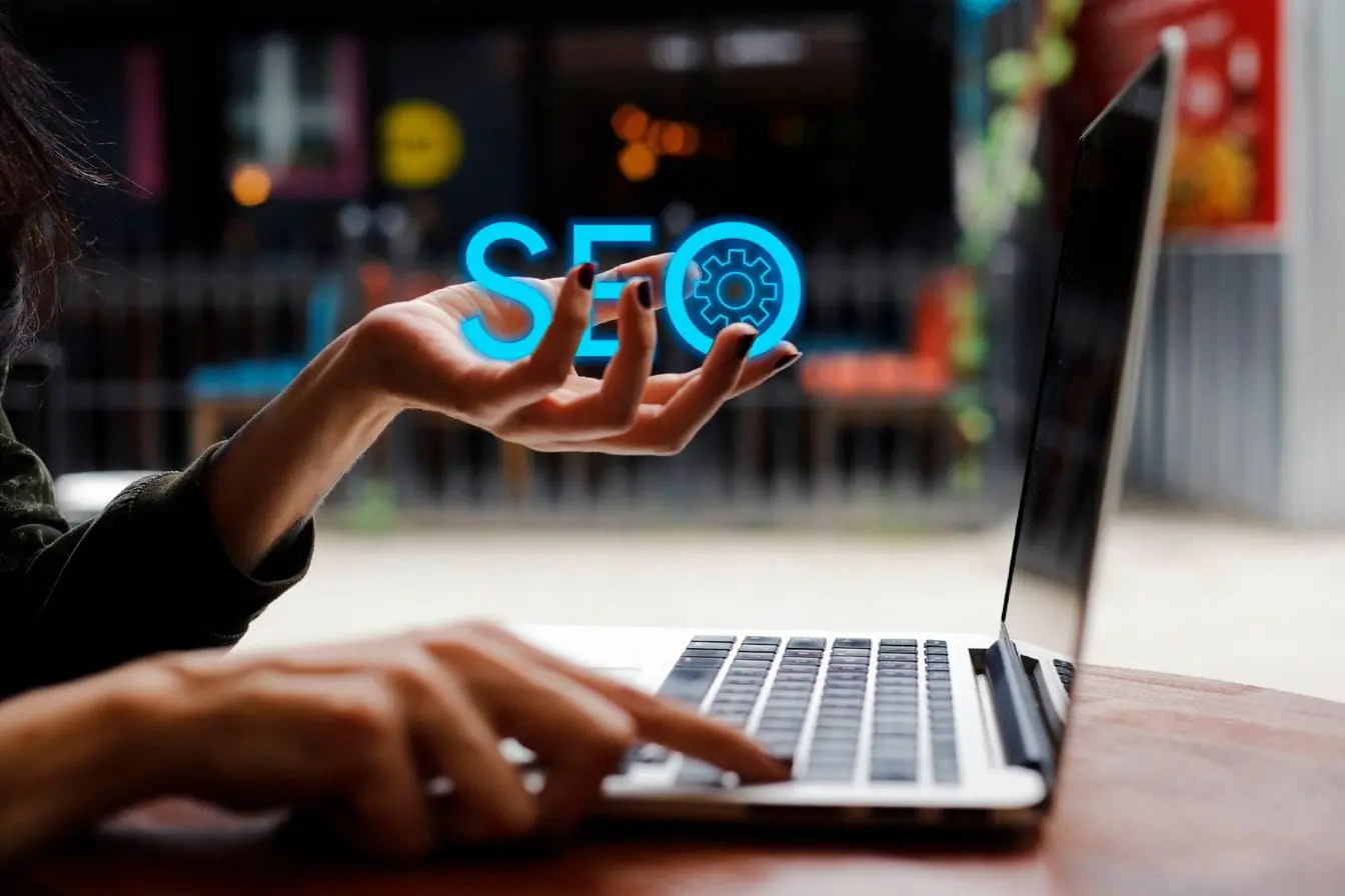 Personne utilisant laptop avec hologramme SEO bleu, reflet d’un cocon sémantique en référencement naturel.