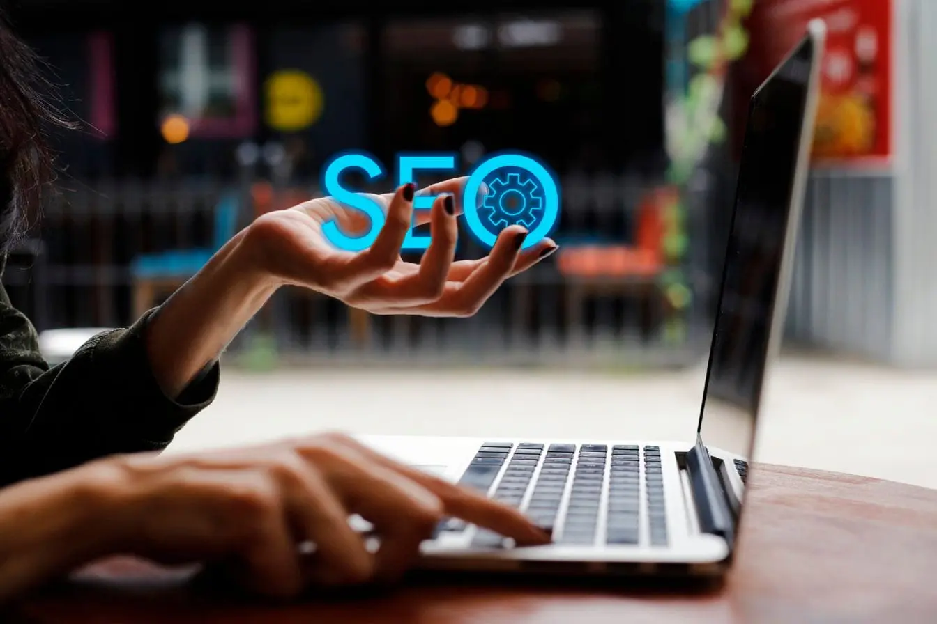 hologramme bleu SEO Personne utilisant un ordinateur portable avec hologramme bleu SEO, image qui illustre le SEO programmatique et l’automatisation des stratégies digitales.