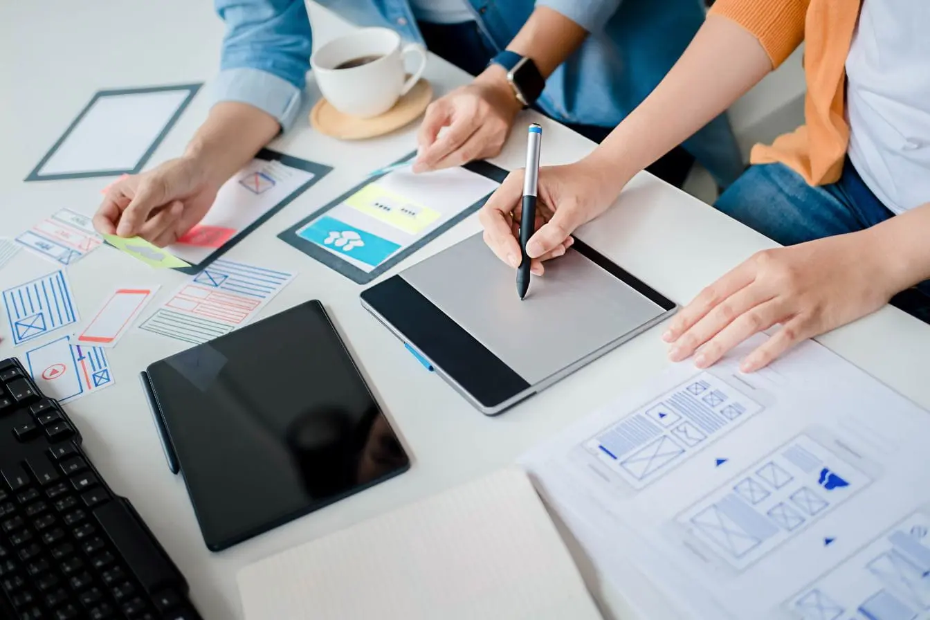 maquettes d’app mobile Deux personnes travaillent sur maquettes d’app mobile avec tablette et croquis, image qui illustre la réflexion entre GraphQL et REST pour concevoir une API.