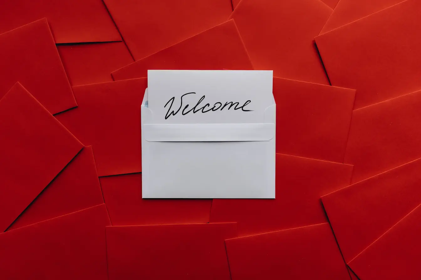 emails de bienvenue Enveloppe blanche ouverte révélant carte Welcome posée sur fond rouge, reflet d’une séquence d’emails de bienvenue engageante.