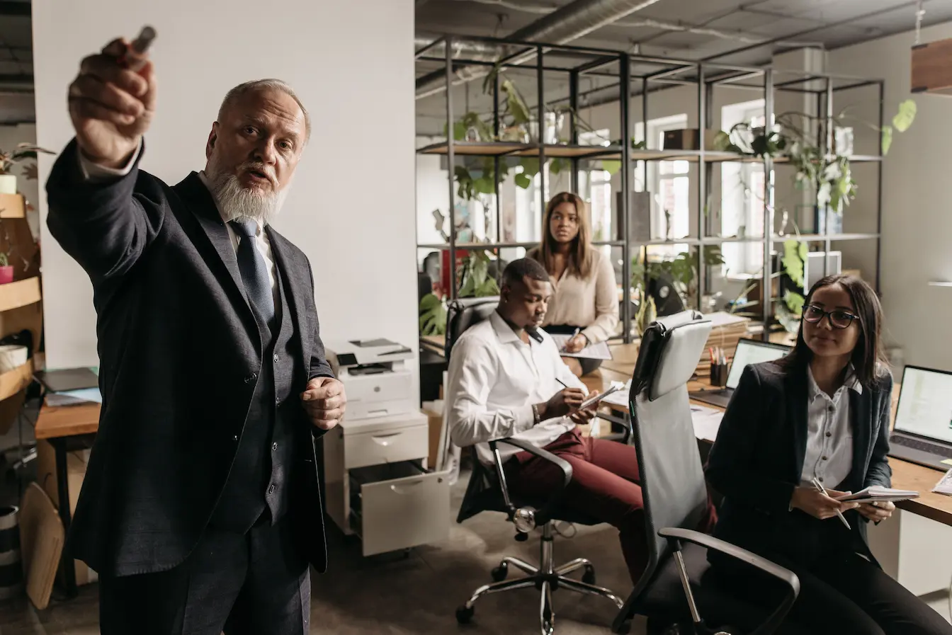 Manager en costume noir présentant devant collègues assis avec ordinateurs, symbole des échanges pour comprendre la différence entre marketing B2B2C et B2B classique.
