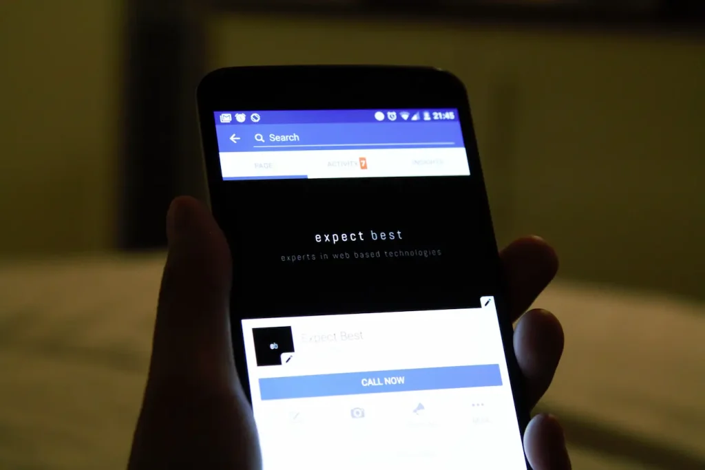 Personne tenant smartphone affichant page Facebook professionnelle, reflet des interactions invisibles et privées du Dark Social.