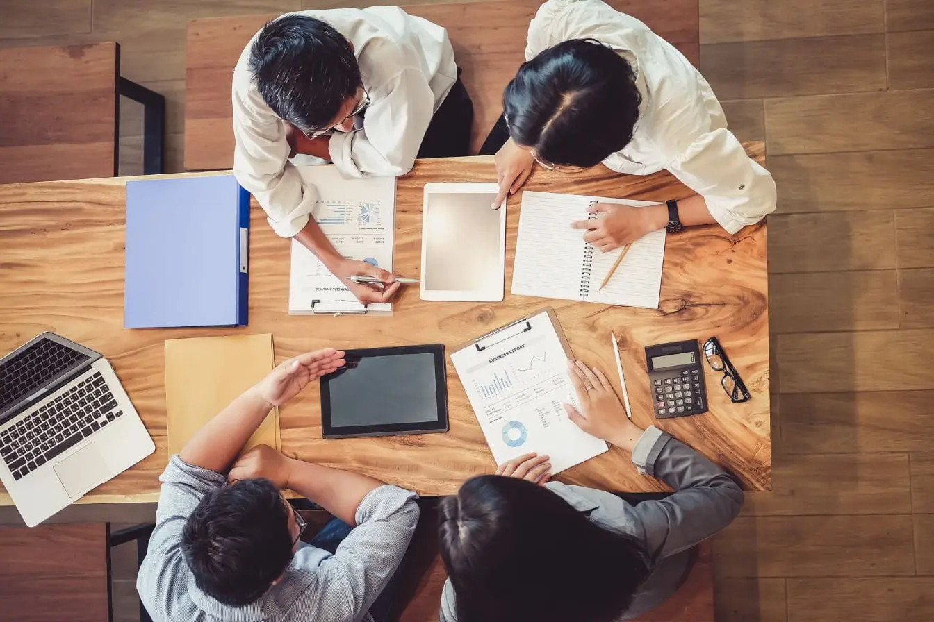 pull marketing Quatre personnes autour d’une table avec graphiques et ordinateurs, reflet d’une discussion sur push et pull marketing