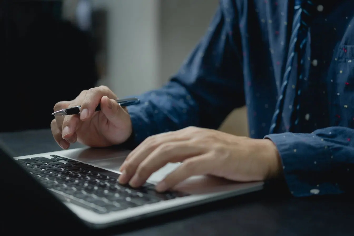 rédiger une meta description Mains tapant sur clavier d’ordinateur portable avec stylo en main, reflet du travail de rédaction d’une meta description efficace.