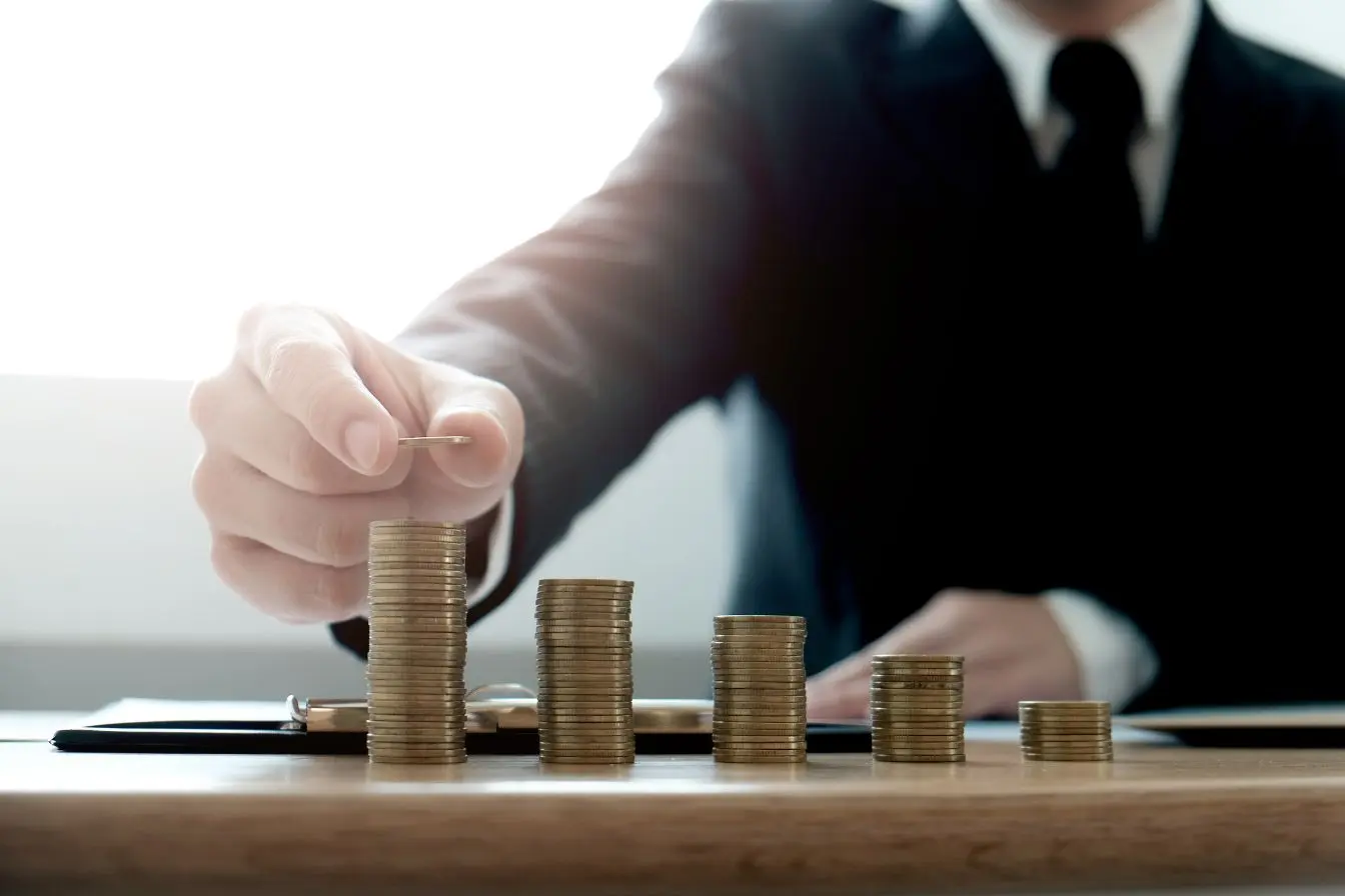 chiffre d’affaires Personne en tenue professionnelle empilant des pièces de monnaie sur un bureau, illustrant la différence entre chiffre d’affaires élevé et marge réellement dégagée