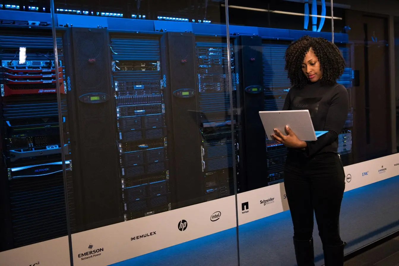 Une technicienne utilisant un ordinateur portable devant de grands serveurs informatiques, idéale pour illustrer la différence entre cloud public et cloud privé.