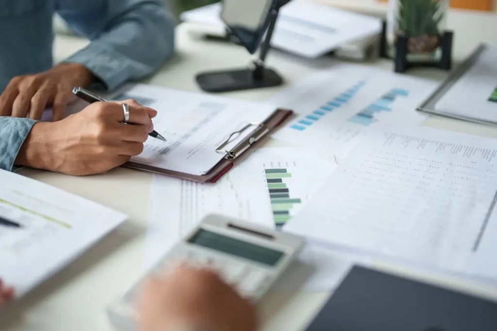 Personne analysant des documents financiers et des graphiques sur un bureau, illustrant la différence entre chiffre d’affaires réalisé et marge réellement conservée