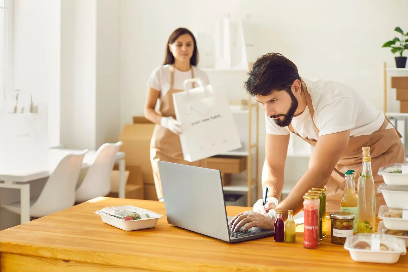 franchise commerciale Deux entrepreneurs organisent des commandes alimentaires dans un local professionnel, illustrant le fonctionnement d’une franchise commerciale en pleine activité