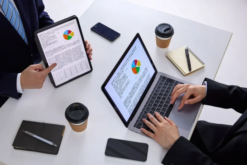 Deux personnes en réunion analysant graphique coloré sur tablette et ordinateur, symbole des stratégies de holding dans une entreprise.
